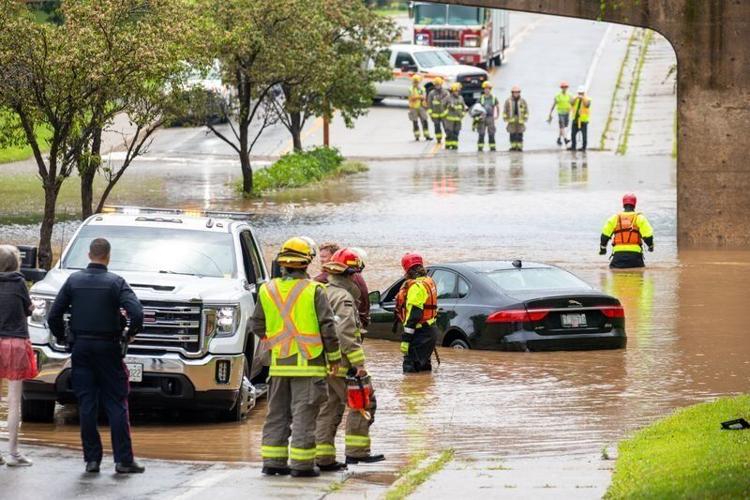 Emergency service workers respond to a flooded street in St. Catharines, Ontario, where a vehicle is partially submerged.