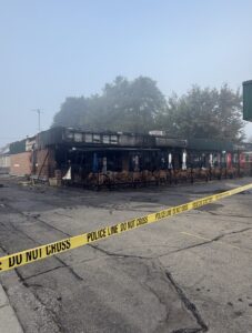 Fire-damaged exterior and patio of Mike’s Place in Chatham, with yellow police tape across the foreground.