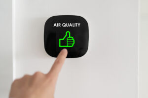 A person touches a wall-mounted air quality display showing a green thumbs-up symbol.