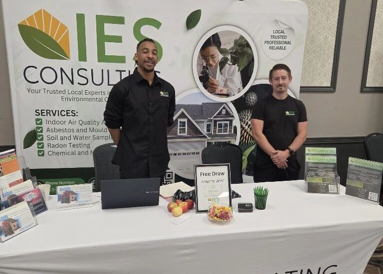 Two IES Consulting representatives stand behind a branded exhibition table with brochures and environmental testing information.
